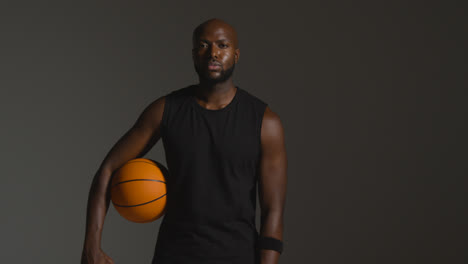 Studioporträtaufnahme-Eines-Männlichen-Basketballspielers,-Der-Vor-Dunklem-Hintergrund-Den-Ball-Unter-Dem-Arm-Hält